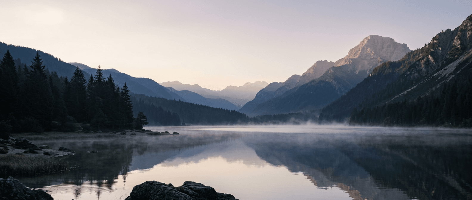 A still alpine lake at dawn, mist over the water and a distant summit catching soft light